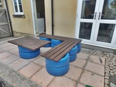 a wooden bench sitting on top of a stone floor next to blue barrels and windows