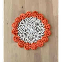 an orange and white crocheted doily on a wooden floor