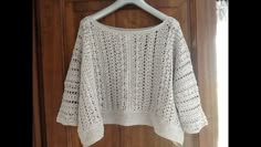 a white crocheted sweater hanging on a wooden hanger in front of a door