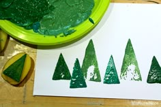 a green plate with some trees on it next to two pieces of paper that have been cut out