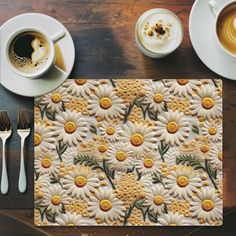 a place mat with yellow and white flowers on it next to two cups of coffee