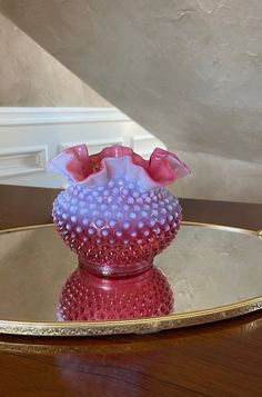 a pink and purple vase sitting on top of a wooden table next to a mirror