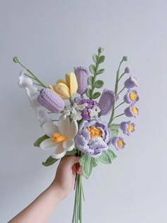 a hand holding a crocheted bouquet of flowers in front of a white wall