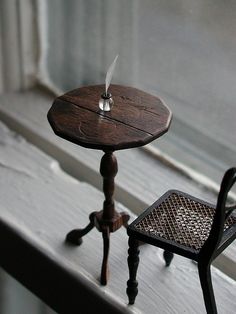 a small wooden table with a candle on it sitting next to a chair in front of a window