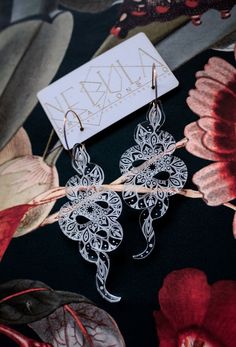 two pairs of earrings sitting on top of a flowery table cloth next to a card