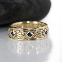 a gold wedding band with blue sapphires on the side and a rock in the background