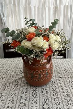 a vase filled with white and orange flowers on top of a table next to a window