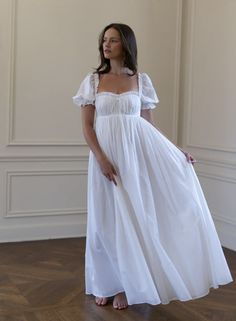 a woman wearing a white dress standing in a room with wood flooring and walls