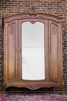 an ornate wooden armoire against a brick wall in front of a rug and mirror