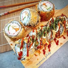 several sushi rolls on a wooden board with chopsticks next to them and ketchup