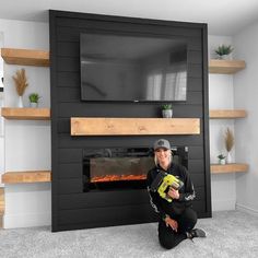 a man kneeling down in front of a fireplace with a tv on it's wall