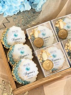 four cupcakes are in a box on a table with blue flowers and lace