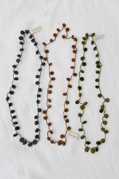 three necklaces with different colored beads on white cloth background, one is black and the other is green