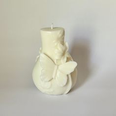 a candle that is sitting in front of a white vase with a butterfly on it