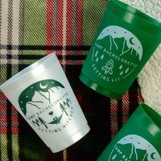 three green cups sitting next to each other on top of a plaid table cloth and blanket