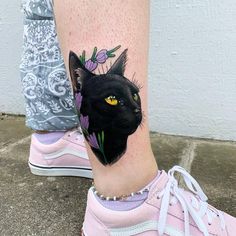 a black cat with yellow eyes and flowers on the leg