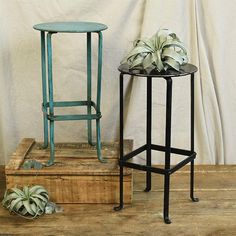 two metal stools sitting next to each other on top of a wooden box filled with plants