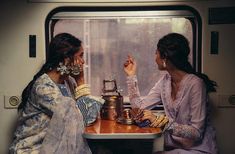 two women sitting at a table on a train looking out the window with rain coming down