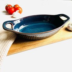 a blue dish sitting on top of a wooden cutting board next to garlic and tomatoes