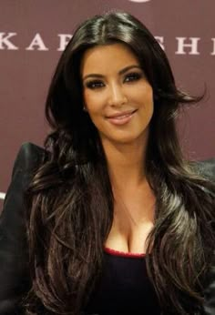 a woman with long hair sitting in front of a sign and posing for the camera