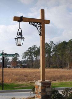 a wooden cross with a light hanging from it's side in front of a grassy field