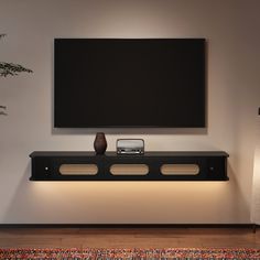 a flat screen tv mounted to the side of a wall next to a vase and lamp