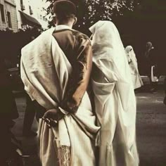 two people dressed in white standing next to each other on a street with trees and buildings behind them