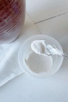 a spoon full of cream sitting on top of a plastic container next to a white cloth