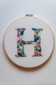 the letter h is made up of flowers and has been stitched into an embroidery hoop