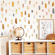 a white dresser topped with baskets next to a wall covered in colorful paint drops on it