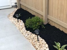 some plants and rocks in front of a wooden fence on the side of a house