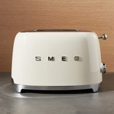 a white toaster sitting on top of a counter next to a wooden wall with the word smeg written on it