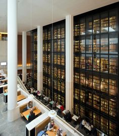 people are sitting at tables and reading books in a large room with high ceilings full of bookshelves