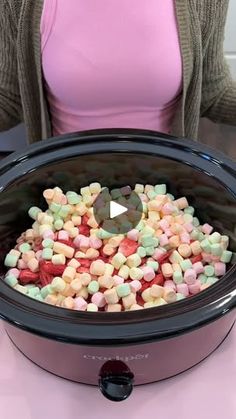 a woman sitting in front of a slow cooker filled with marshmallows