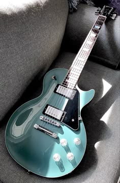 a blue electric guitar sitting on top of a gray couch next to a black pillow