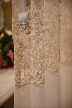 sheer curtains with lace on them are hanging in front of a flower vase and window sill