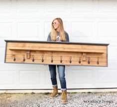 a woman holding a large wooden coat rack with hooks on the front and bottom, while standing in front of a garage door