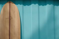 a wooden surfboard leaning up against a blue wall with shadows on the board and bottom