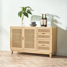 a wooden sideboard with two bottles and a bowl on top, next to a potted plant