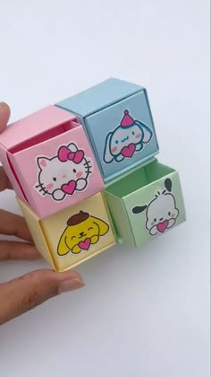 a hand is holding four small boxes with hello kitty faces on them, one has a bow and the other has an ear