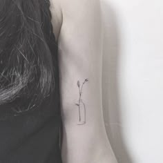 a woman's arm with a small flower in a vase tattoo on the left inner arm