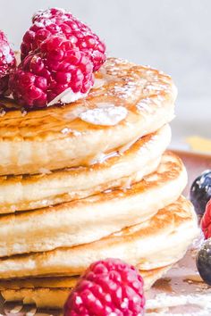 a stack of pancakes topped with raspberries and powdered sugar