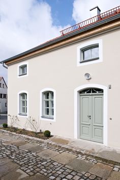 a white house with two doors and windows on the side walk next to a cobblestone street