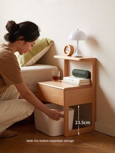 a woman kneeling down next to a small table with a lamp on top of it