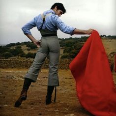 a man holding onto a red cloth while standing on top of a dirt field