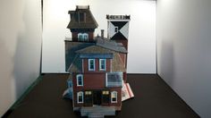 a paper model of a house on display in a room with white walls and black flooring