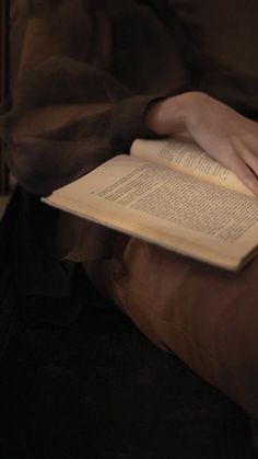 a person sitting down reading a book with their hands on top of the open book