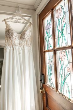 a wedding dress hanging in front of a stained glass window with the bride's name on it