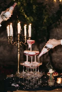 a person pouring wine into glasses on top of a table with candles in the background