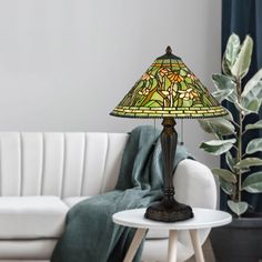 a table lamp sitting on top of a white table next to a couch and potted plant